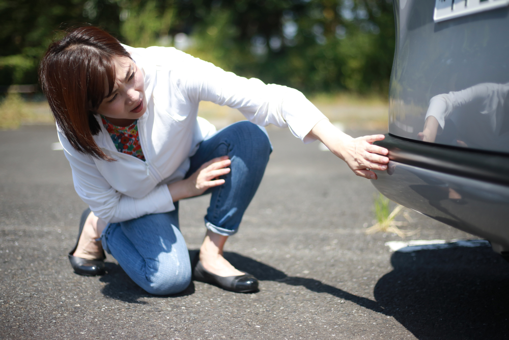 A woman examines her car after a hit and run.